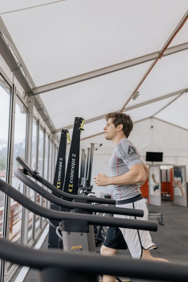 A man running on a treadmill in a bright gym with large windows