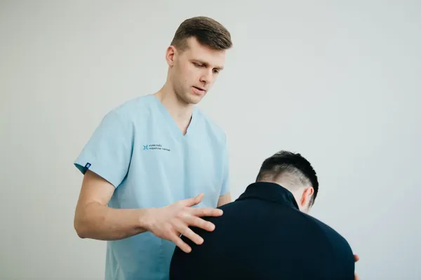 Ethan Brooks in light-blue scrubs checking a patient's back posture