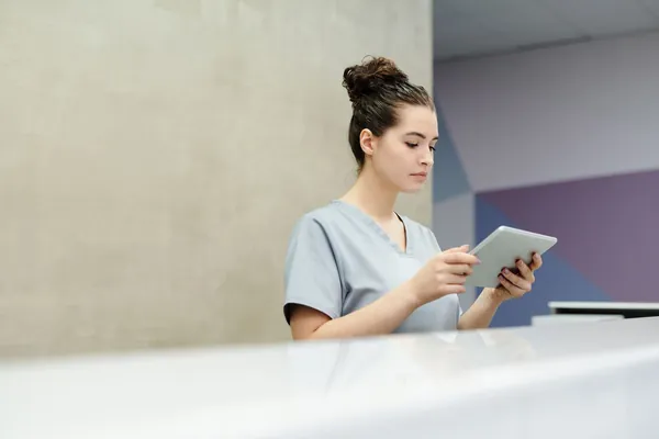 Grace Holloway in scrubs reading a tablet at the clinic front desk